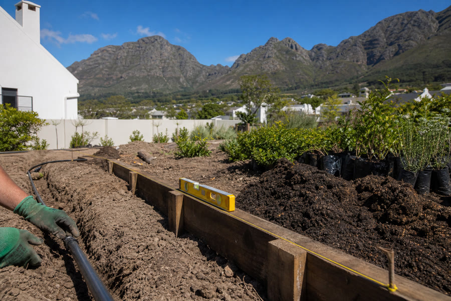 Irrigation pipe being laid in a trench beside a new sleeper retaining edge on a Helderberg garden build.